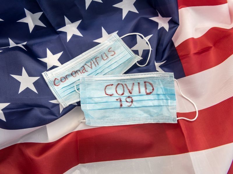 american flag with two blue medical face masks on top that say coronavirus and covid-19