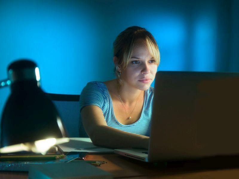 blond woman looking at her laptop at her desk in the dark