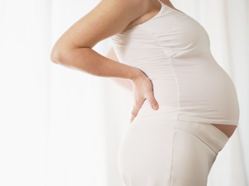 pregnant woman in all white outfit with her hands on her lower back