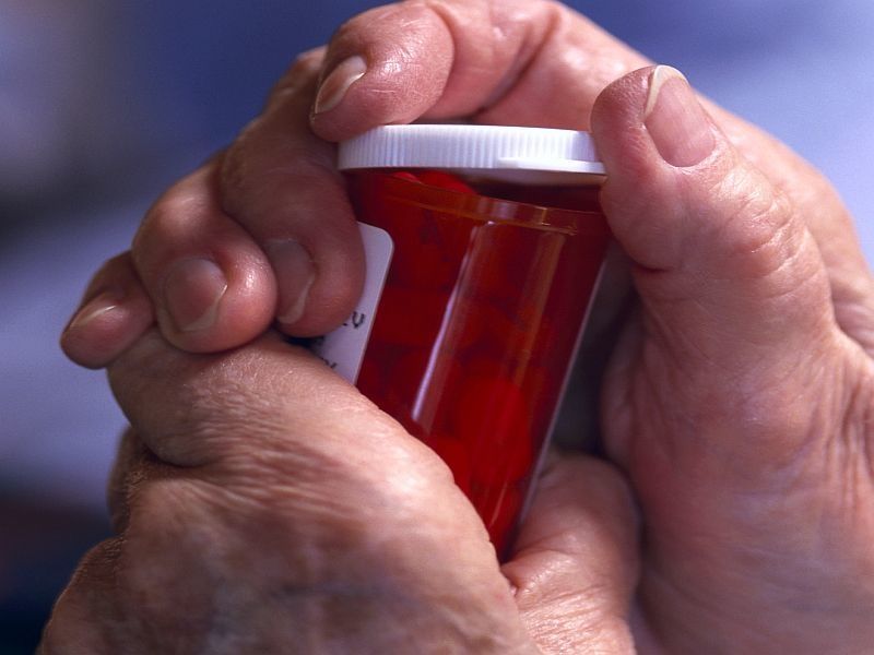 older person's hands trying to take lid off the top of an orange prescription bottle