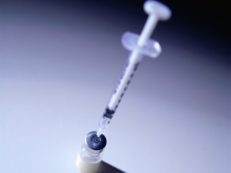 needle and syringe sticking out of a clear glass vial of vaccine liquid