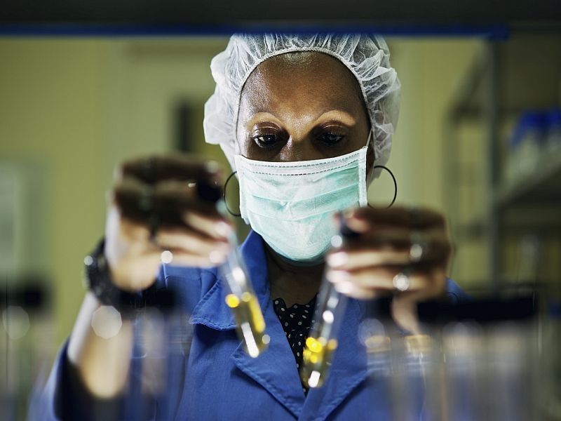 woman laboratory worker holding up two test tubes with yellow liquid inside